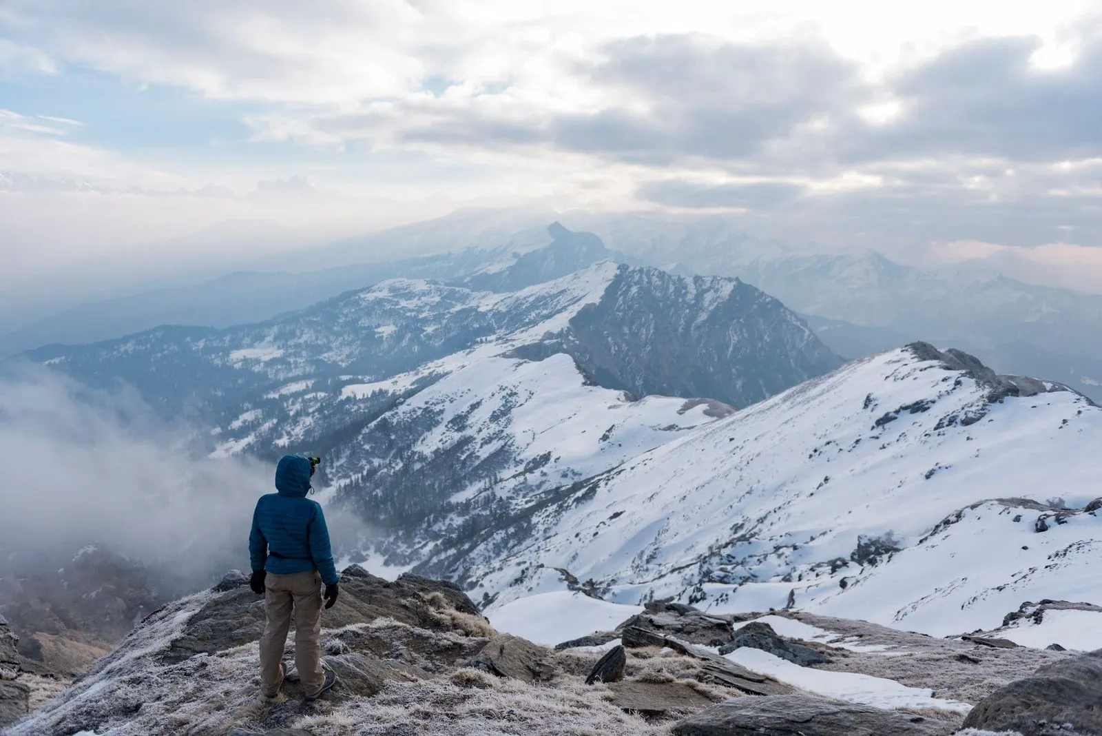 En vandrare står på en bergstopp med snötäckta fjäll i bakgrunden