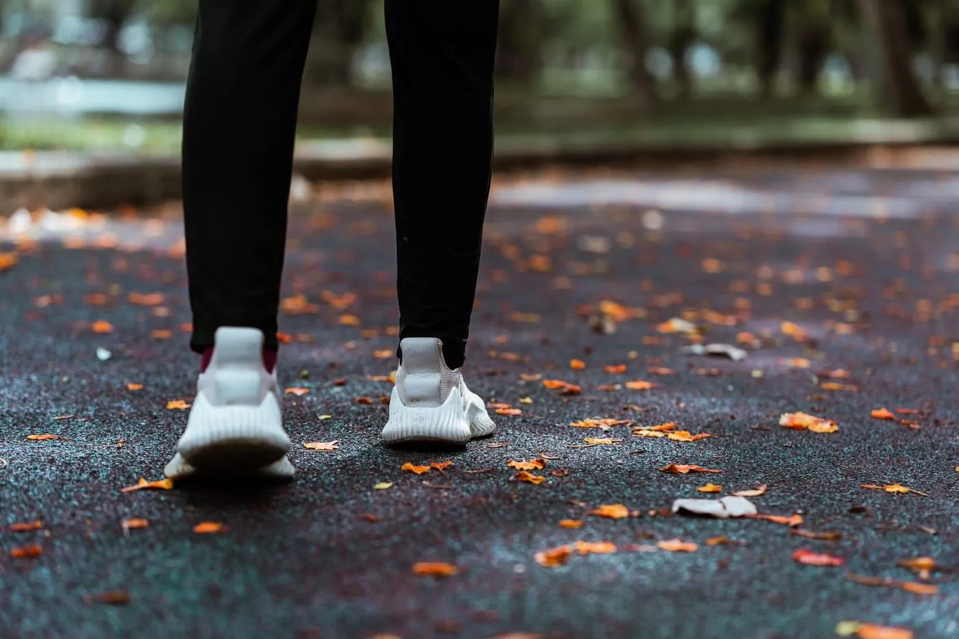 Ben i vita gympaskor som går på en asfaltsstig täckt av höstlöv.
