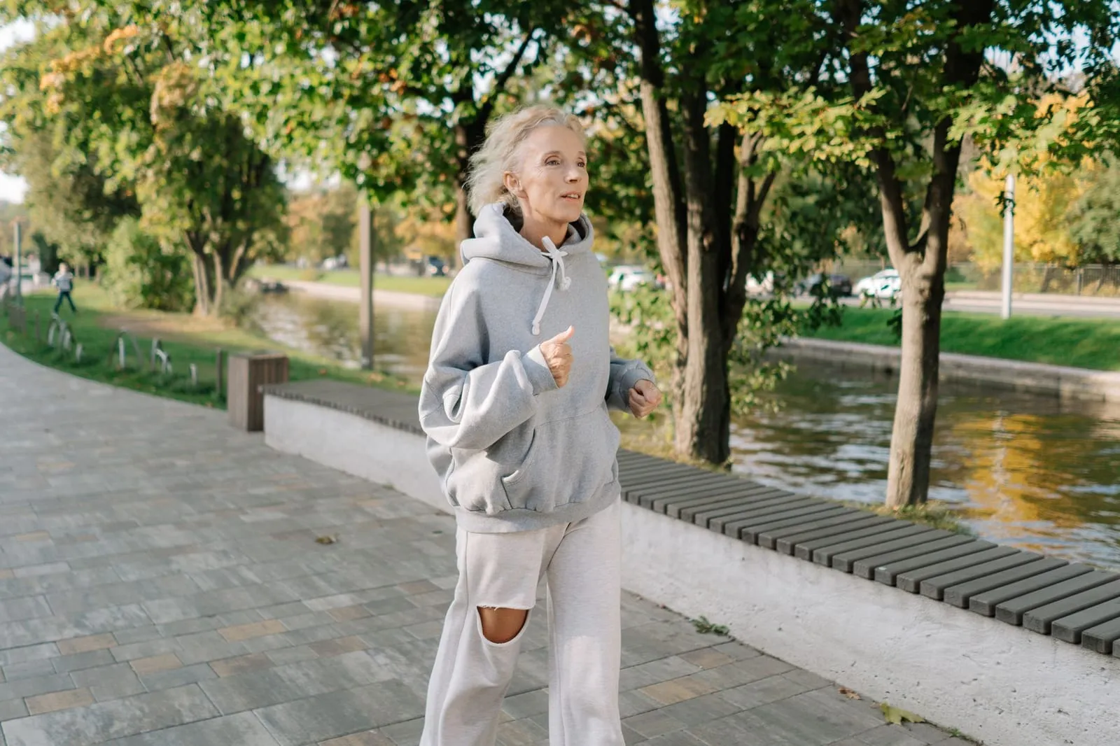 Äldre kvinna som joggar i lugnt tempo längs en gångväg vid en kanal.