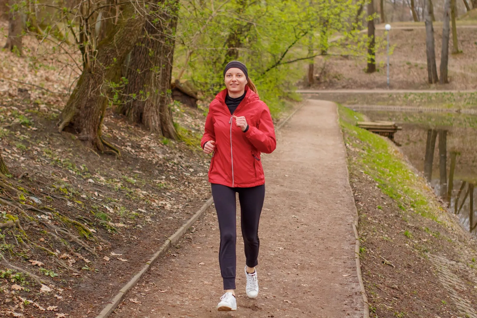 Kvinna i röd jacka som joggar lugnt på en skogsstig.