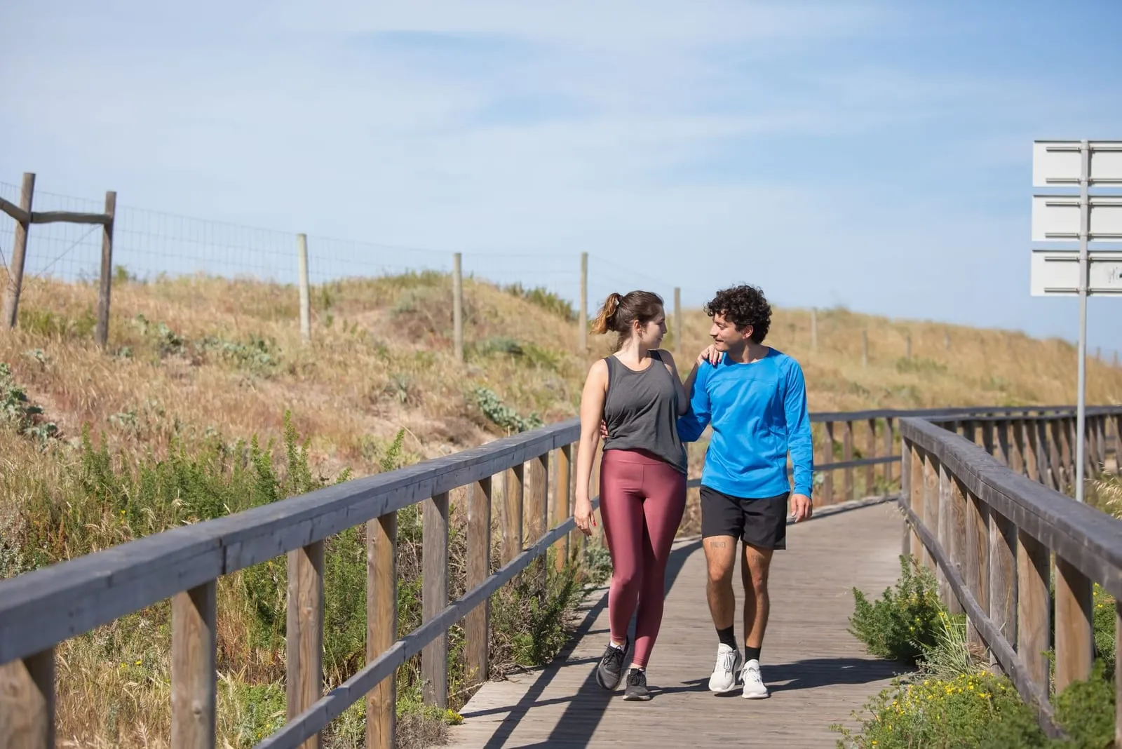 Par i träningskläder promenerar på en brygga i en naturmiljö.