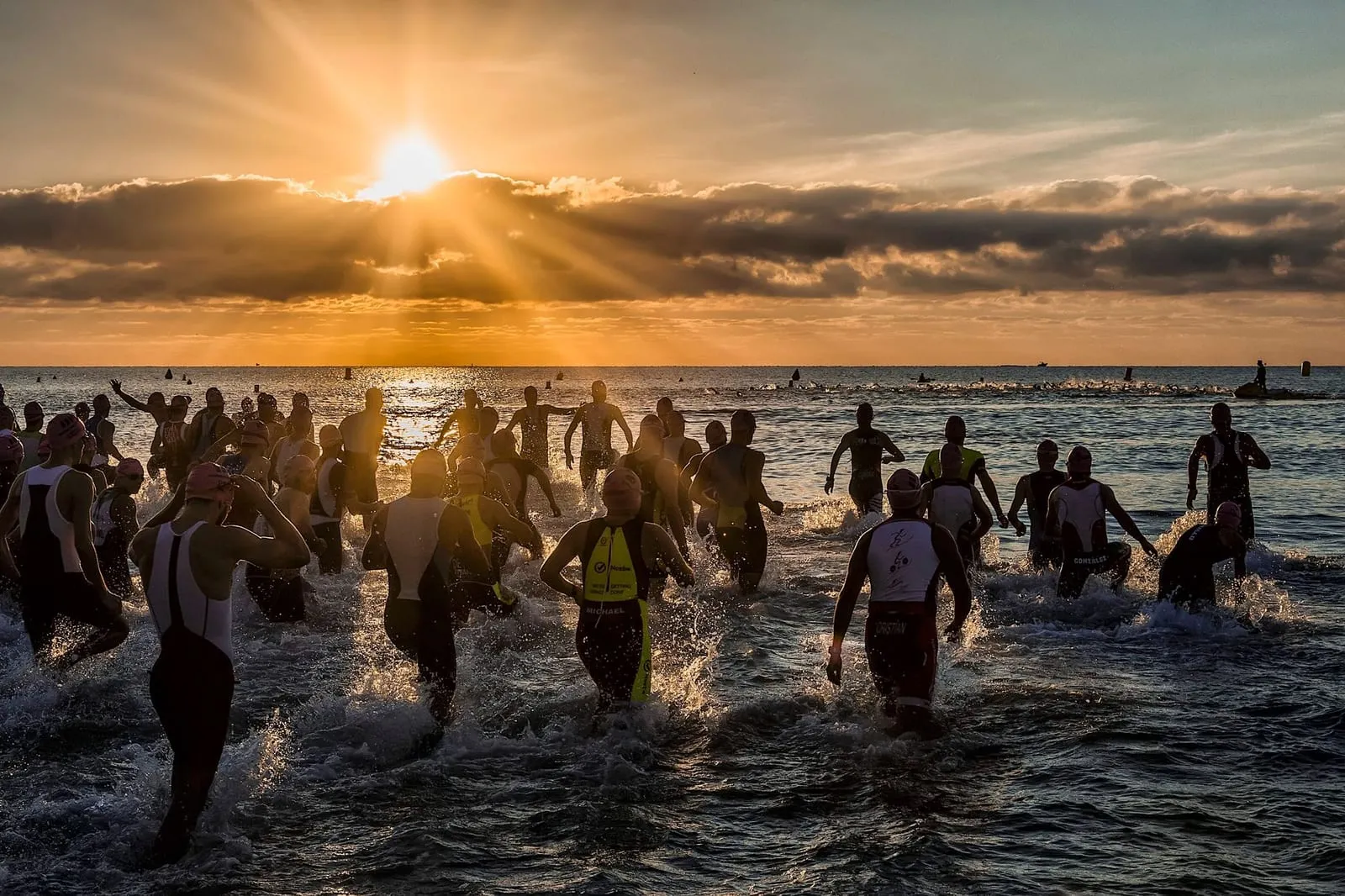 Deltagare i ett triathlon springer ut i havet vid soluppgång.