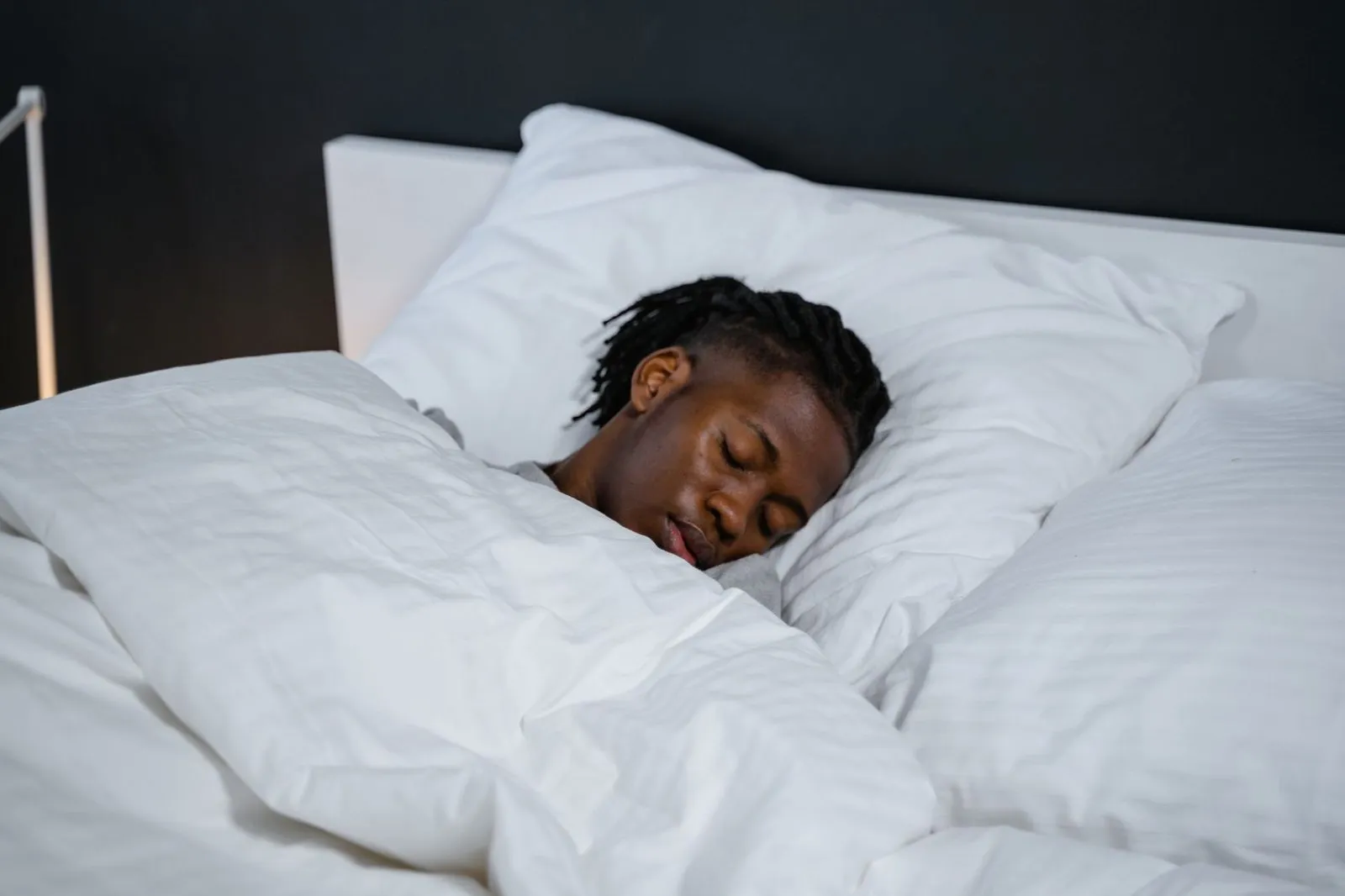 En ung man sover i en säng med vita lakan