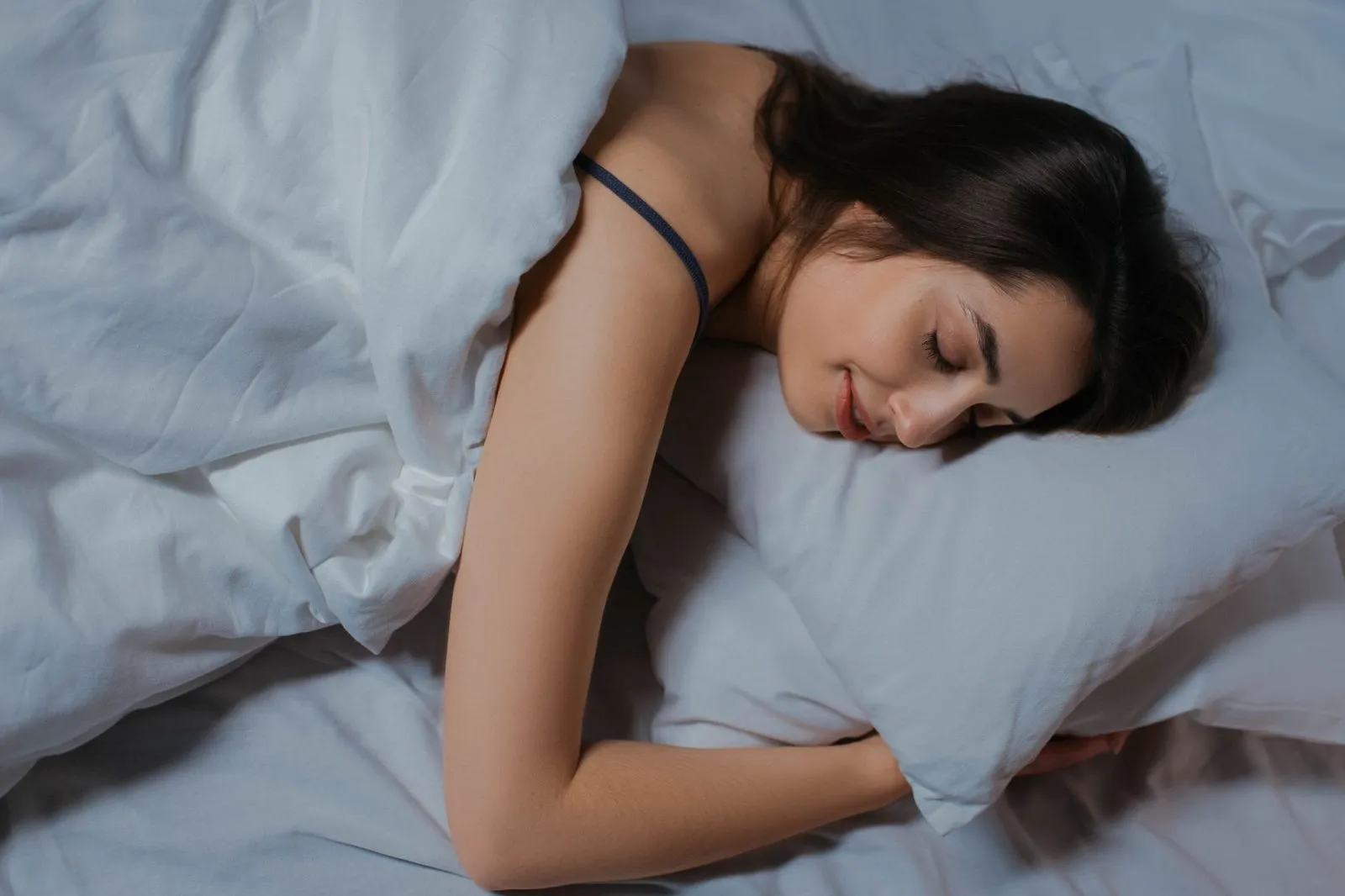 En kvinna sover på sidan i en säng med vita lakan