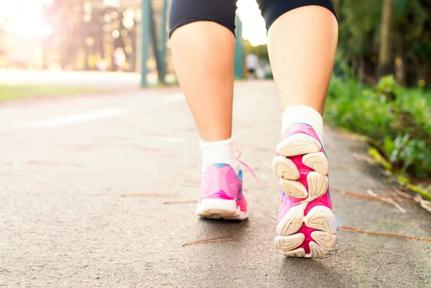 Närbild på ben i rosa joggingskor som går på en asfalterad stig.