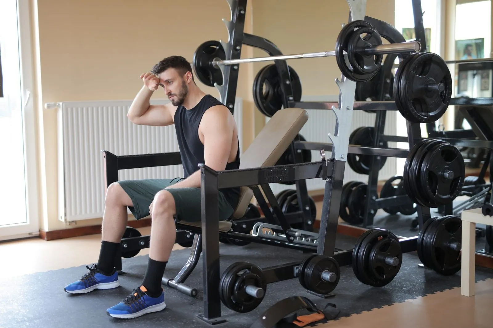 Man som sitter nedhukad på en bänk i ett gym och torkar pannan.