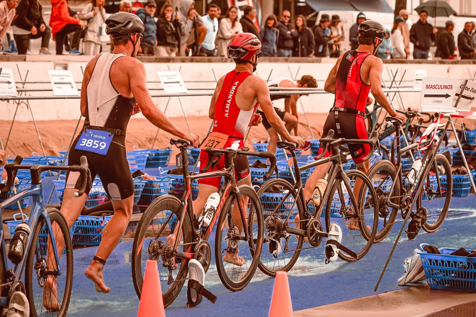 Triathleter går med sina cyklar genom växlingszonen efter simningen.