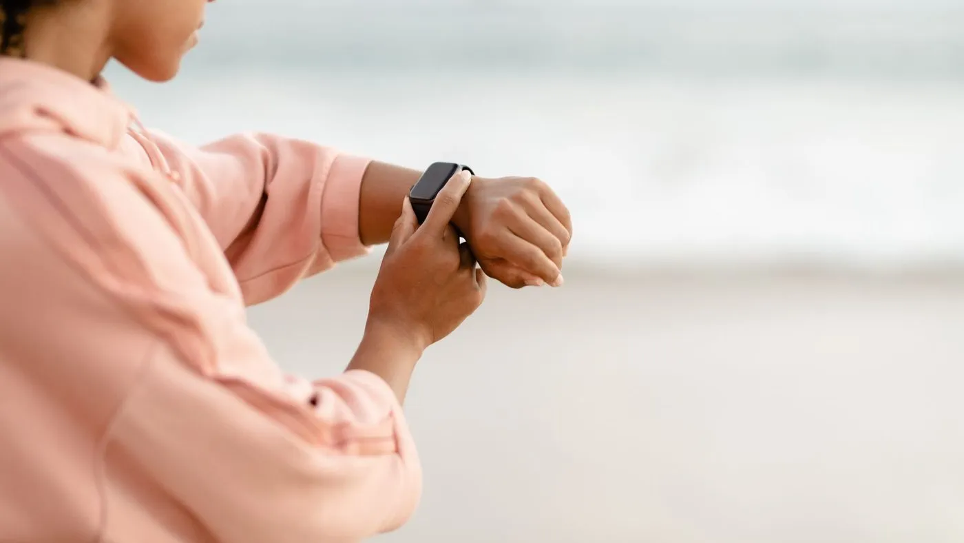 Kvinna i rosa tröja som tittar på sin sportklocka vid havet