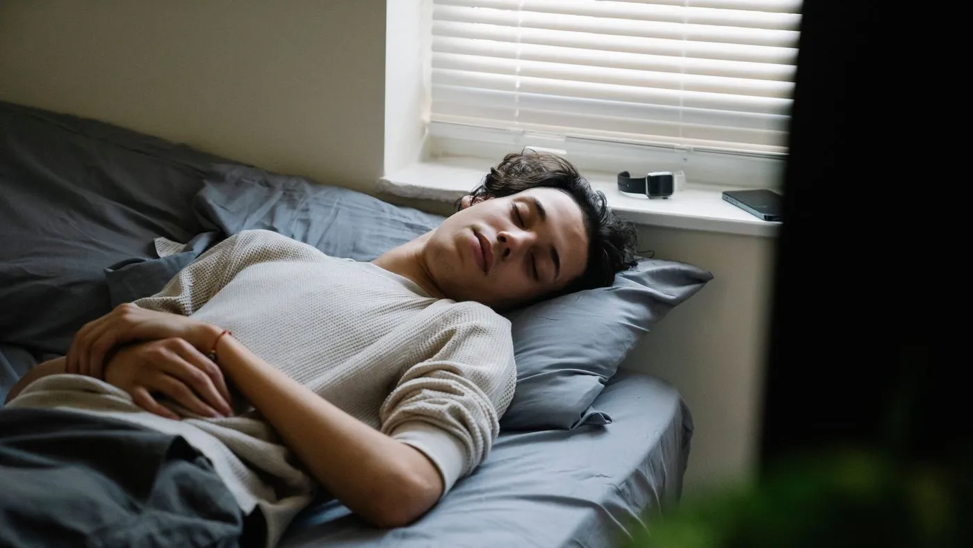 Man som sover lugnt i en säng vid ett fönster med dämpat morgonljus