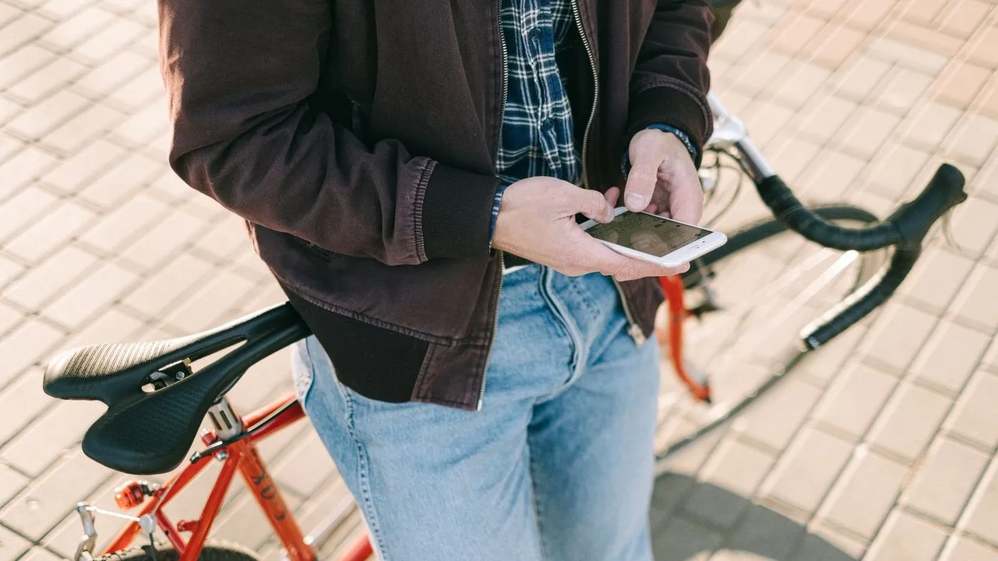 Man som står vid sin röda racercykel och tittar på mobilen efter en tur