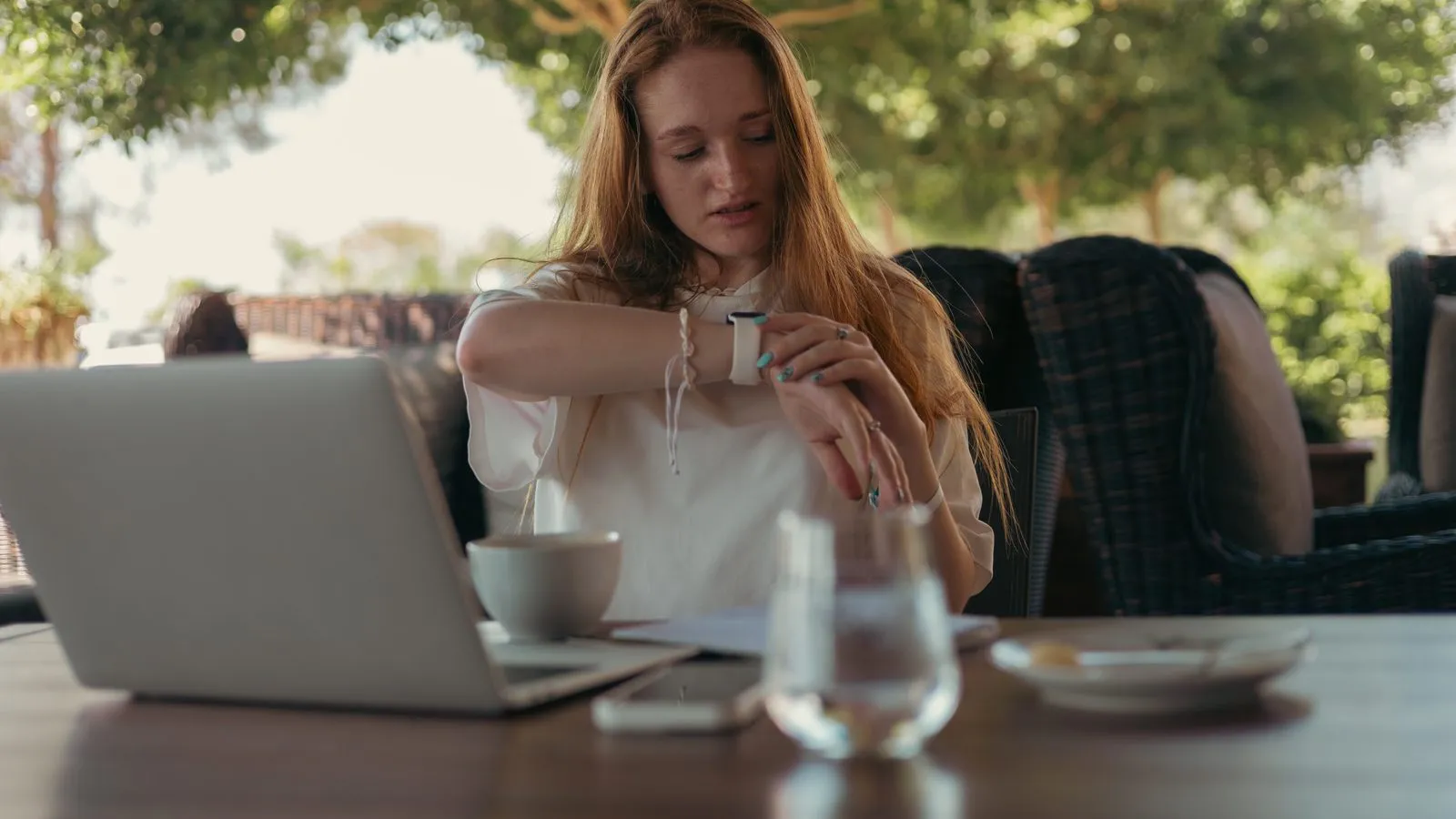Kvinna vid ett cafébord med laptop tittar på klockan på handleden