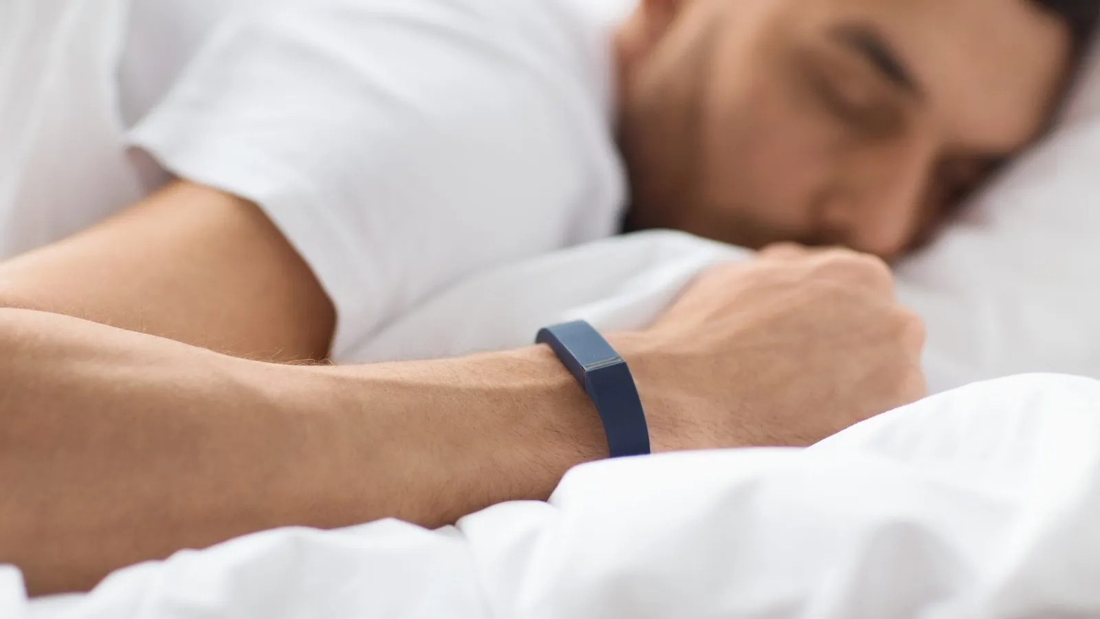 Man sover på sidan med ett blått fitnessarmband runt handleden