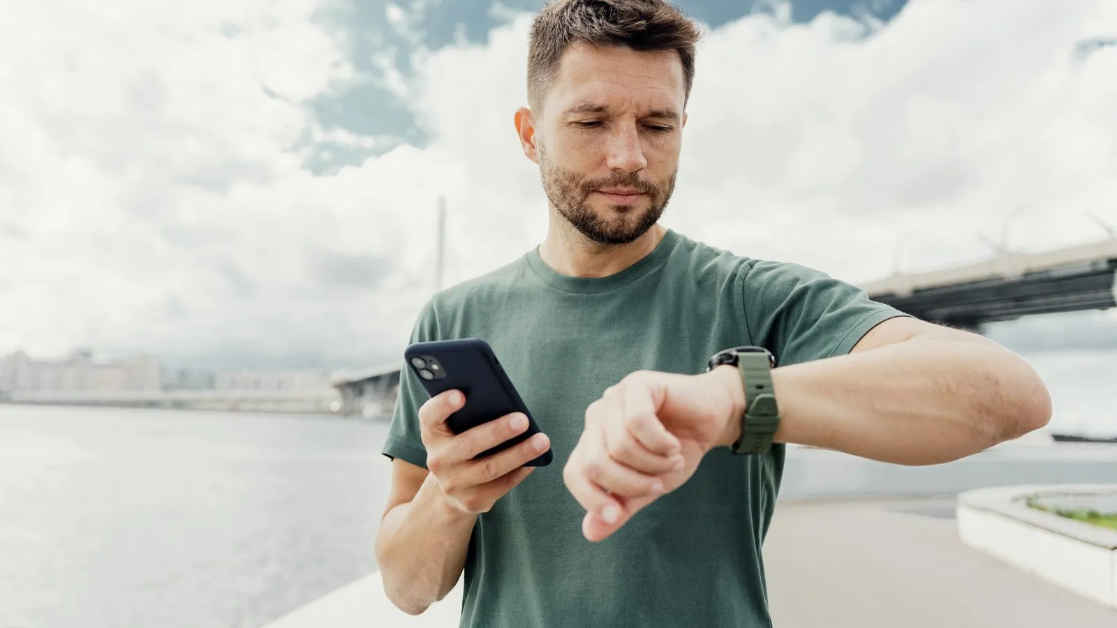 Man utomhus kollar sin klocka med mobilen i handen